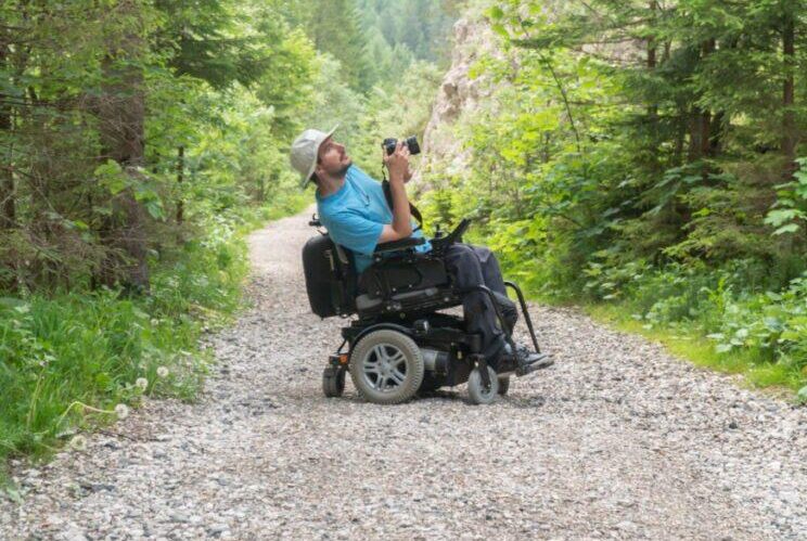 man in powerchair taking a photo on a trail