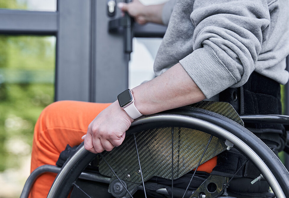 Cropped view of the physically challenged girl moving herself at the wheelchair and opening doors of the building. Stock photo